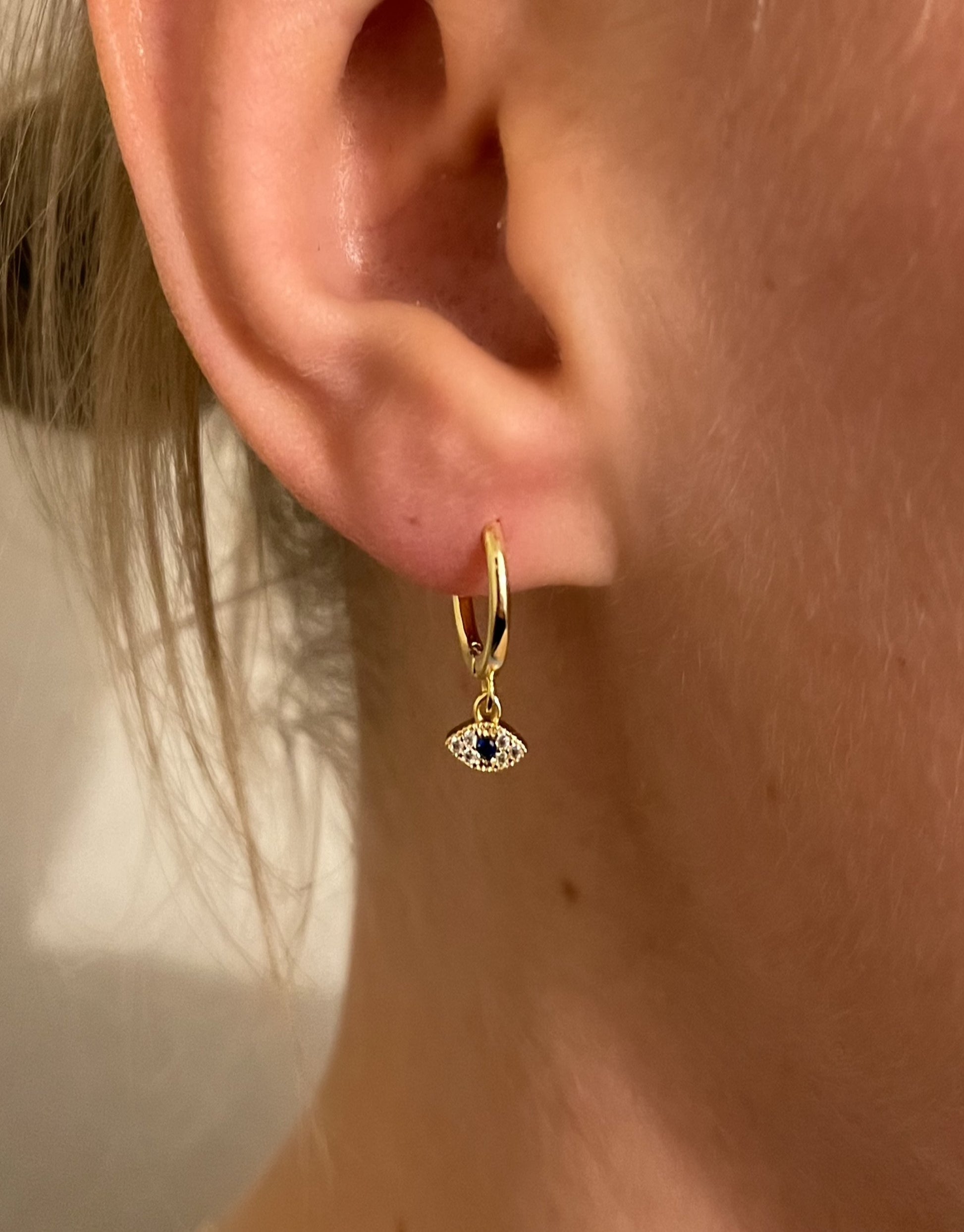 Nazar øreringe i guld med små flotte zircon sten og en blå sten som øje.